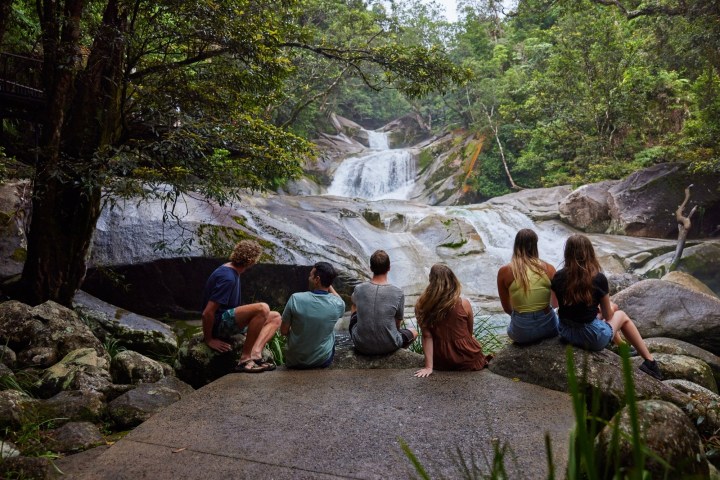Visitors sitting on granite beside a wide cascade on the Atherton Tablelands near Cairns