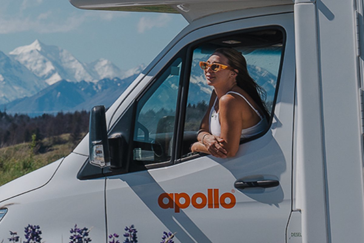 An Apollo campervan with the driver looking out of the window, mountains behind