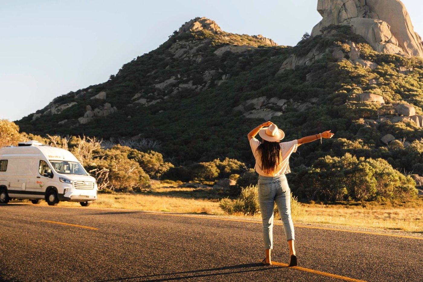 A Britz campervan on a quiet road below a granite peak at golden hour