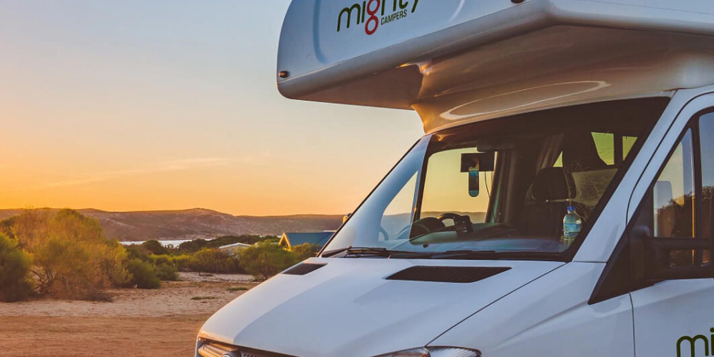 A Mighty campers motorhome parked in coastal scrub as the sun sets behind it